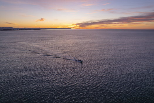 Aerial view of a small boat cruising on the calm sea during a vibrant sunset near Praia dos Arrifes in Faro District Portugal. Aerial view of a small boat cruising on the calm sea during a vibrant sunset near Praia dos Arrifes in Faro District Portugal.