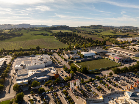 Aerial view of commercial buildings with solar panels a soccer field and parking lots surrounded by green hills in Ancona Marche Italy. Aerial view of commercial buildings with solar panels a soccer field and parking lots surrounded by green hills in Ancona Marche Italy.