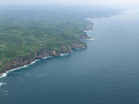 Aerial view of Sedahan Beach where rugged green cliffs meet the deep blue sea under a hazy sky Gunungkidul Regency Special Region of Yogyakarta Indonesia. Aerial view of Sedahan Beach where rugged green cliffs meet the deep blue sea under a hazy sky Gunungkidul Regency Special Region of Yogyakarta Indonesia.