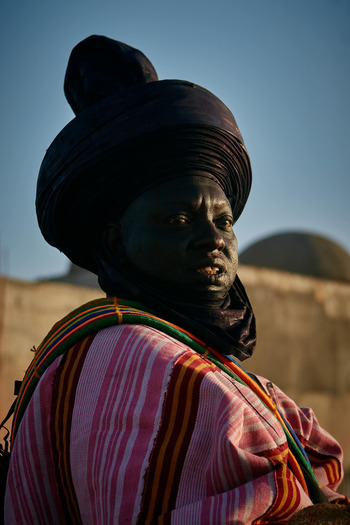 Zaria city Nigeria 22 March 2026 View of a regal man in a dark turban and vibrant striped robe his features illuminated by warm light against the soft blur of an ancient dome. Zaria city Nigeria 22 March 2026 View of a regal man in a dark turban and vibrant striped robe his features illuminated by warm light against the soft blur of an ancient dome.