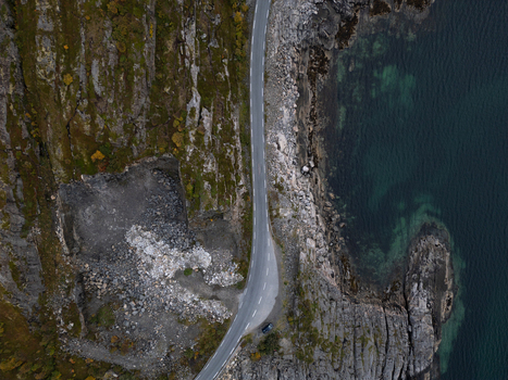 Aerial view of a coastal road winding between steep rocky cliffs and the turquoise sea at Rorvikstranda in Henningsvaer Nordland Norway.