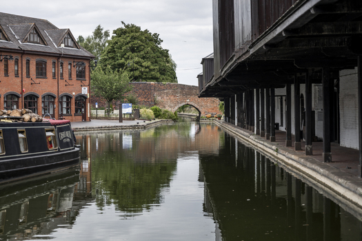 Coventry England United Kingdom 20 July 2026 View of the historic Coventry Canal Basin with a narrowboat moored alongside brick buildings and a stone arch bridge under a cloudy sky.