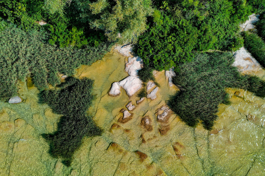 Aerial view of Jamaica Beach featuring flat limestone rocks under clear water and lush green vegetation in Sirmione Lombardia Italy.