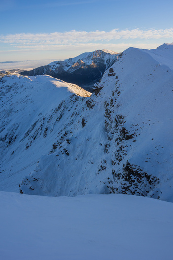 View of Ornak mountain peak in the Western Tatras covered in deep snow under a clear blue sky with golden sunlight on the ridges in Tatra County Lesser Poland Voivode Poland. View of Ornak mountain peak in the Western Tatras covered in deep snow under a clear blue sky with golden sunlight on the ridges in Tatra County Lesser Poland Voivode Poland.