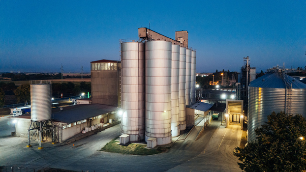 Aerial view of an industrial grain silo facility illuminated at twilight with large metal storage tanks and a paved yard in Sremska Mitrovica Vojvodina Serbia. Aerial view of an industrial grain silo facility illuminated at twilight with large metal storage tanks and a paved yard in Sremska Mitrovica Vojvodina Serbia.
