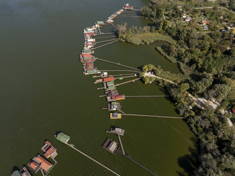 Aerial view of Bokodi Floating Village with its colorful wooden houses on stilts connected by long wooden walkways over the calm lake water in Oroszlany Hungary. Aerial view of Bokodi Floating Village with its colorful wooden houses on stilts connected by long wooden walkways over the calm lake water in Oroszlany Hungary.