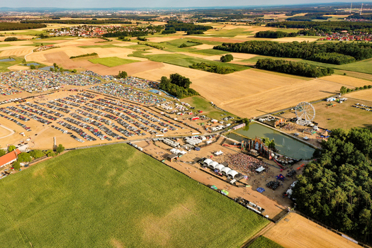 Herzogenaurach Germany 22 July 2022 Aerial view of the Open Beatz Festival featuring stages a Ferris wheel and a large parking area surrounded by agricultural fields and forests. Herzogenaurach Germany 22 July 2022 Aerial view of the Open Beatz Festival featuring stages a Ferris wheel and a large parking area surrounded by agricultural fields and forests.