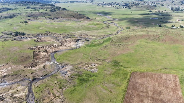 Aerial view of a winding riverbed showing signs of soil erosion and gullies across green rolling hills and rural landscapes in Pietermaritzburg KwaZulu Natal South Africa.