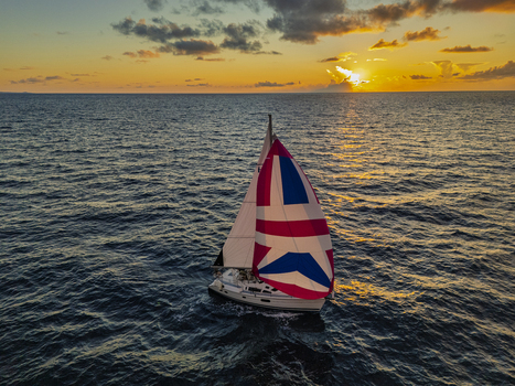 Aerial view of a sailboat with a colorful Union Jack spinnaker sail gliding across the deep blue ocean waters during a vibrant sunset Waimea Hawaii United States. Aerial view of a sailboat with a colorful Union Jack spinnaker sail gliding across the deep blue ocean waters during a vibrant sunset Waimea Hawaii United States.