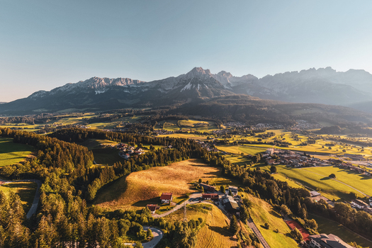 Aerial view of the Wilder Kaiser mountain range rising above the lush green meadows forests and scattered farmhouses in the valley of Wilder Kaiser Tirol Austria. Aerial view of the Wilder Kaiser mountain range rising above the lush green meadows forests and scattered farmhouses in the valley of Wilder Kaiser Tirol Austria.