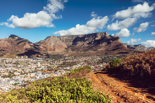 View of Table Mountain overlooking the city skyline with a dirt hiking trail in the foreground under a blue sky in Cape Town Western Cape South Africa. View of Table Mountain overlooking the city skyline with a dirt hiking trail in the foreground under a blue sky in Cape Town Western Cape South Africa.