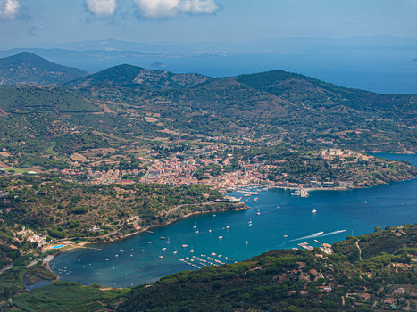 Aerial view of Porto Azzurro harbor with boats in the turquoise bay surrounded by green hills and historic town architecture in Porto Azzurro Toscana Italy.