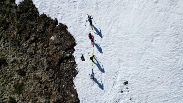 Aerial view of four ski tourers walking in a line on the snowy slopes of Pointe Ronde with long shadows and rocky terrain in Trient Valais Switzerland.