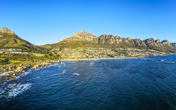 Aerial view of the Twelve Apostles mountain range and coastal suburbs along the Atlantic Ocean with rocky shorelines and clear blue sky in Cape Town Western Cape South Africa.