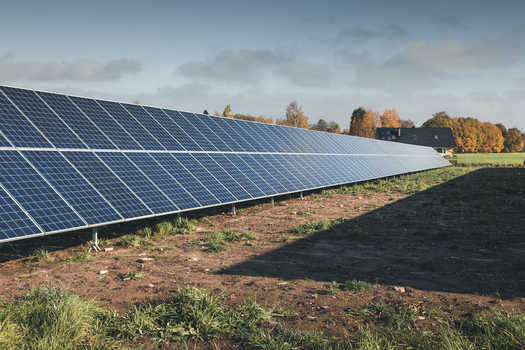 View of a large solar panel array installed in a rural field with autumn trees and a house in the background in Tartu County Estonia. View of a large solar panel array installed in a rural field with autumn trees and a house in the background in Tartu County Estonia.