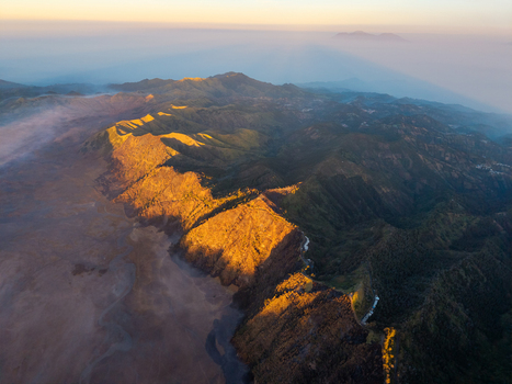 Aerial view of the Podokoyo region near Mount Bromo featuring rugged volcanic terrain deep valleys and golden hour light illuminating the mountain ridges in Tosari East Java Indonesia.