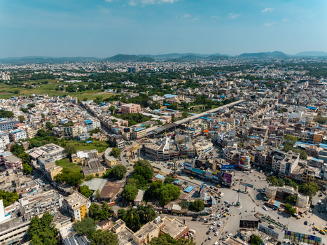 Aerial view of the dense urban landscape of Udaipur featuring intricate street networks buildings and distant hills under a clear blue sky in Udaipur Rajasthan India.