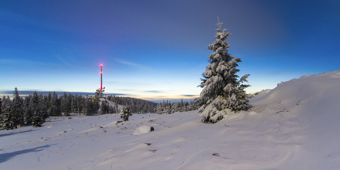 View of a snow covered landscape with a communication tower with red lights and a snow laden pine tree under a vibrant blue sky Schöckl Styria Austria. View of a snow covered landscape with a communication tower with red lights and a snow laden pine tree under a vibrant blue sky Schöckl Styria Austria.