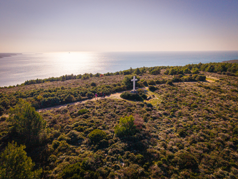 Aerial view of the stark white cross standing prominently atop the verdant hill overlooking the shimmering sea a beacon against the horizon Medulin Istria County Croatia.
