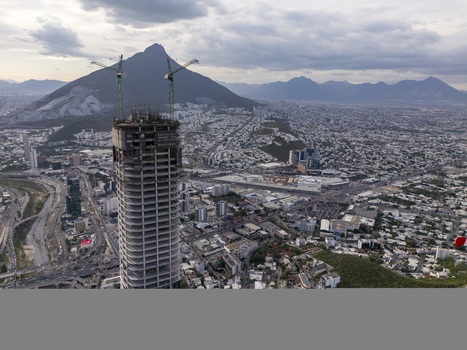 Aerial view of Rise Tower under construction with cranes surrounded by the urban sprawl of Monterrey and the Cerro de la Silla mountain under a cloudy sky. Monterrey Nuevo Leon Mexico. Aerial view of Rise Tower under construction with cranes surrounded by the urban sprawl of Monterrey and the Cerro de la Silla mountain under a cloudy sky. Monterrey Nuevo Leon Mexico.