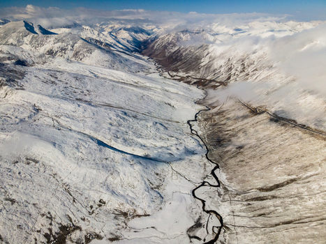 Aerial view of Babusar Pass with snow covered mountain peaks a winding road through a deep valley and thick white clouds under a clear blue sky Babusar KPK Pakistan. Aerial view of Babusar Pass with snow covered mountain peaks a winding road through a deep valley and thick white clouds under a clear blue sky Babusar KPK Pakistan.