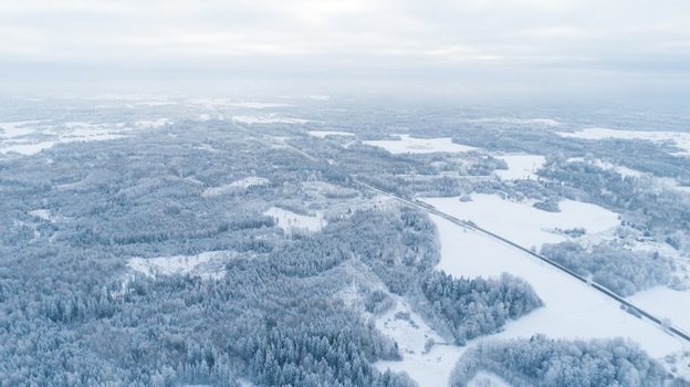 Aerial view of snow covered forests and fields with a road winding through the winter landscape in Latvia. Aerial view of snow covered forests and fields with a road winding through the winter landscape in Latvia.