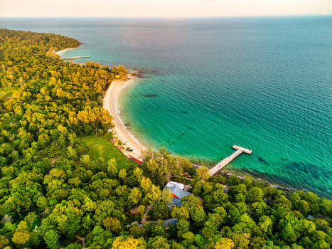 Aerial view of lush green canopy meeting the turquoise sea with a pristine beach and a wooden pier stretching into the water Preah Sihanouk Sihanoukville Cambodia.