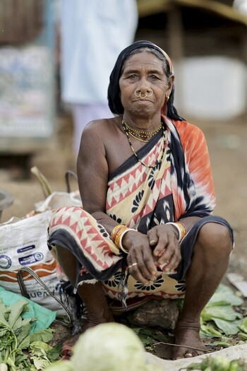 Odisha India 26 March 2026 View of an indigenous woman with a determined gaze adorned in a vibrant patterned sari crouched amidst the bustling market scene. Odisha India 26 March 2026 View of an indigenous woman with a determined gaze adorned in a vibrant patterned sari crouched amidst the bustling market scene.