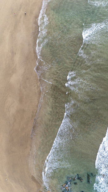Aerial view of Antilla beach with gentle waves washing onto the golden sand and rocky formations visible in the clear water in Gipuzkoa Basque Country Spain.