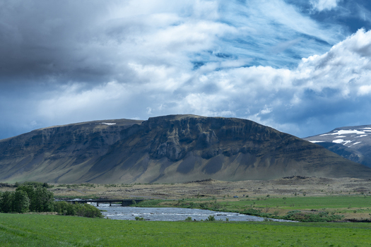 View of the rugged mountains and a flowing river under a dramatic cloudy sky in Hvalfjordur Iceland. View of the rugged mountains and a flowing river under a dramatic cloudy sky in Hvalfjordur Iceland.