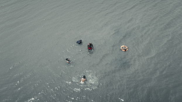 Aerial view of people swimming in the greyish blue ocean water with one person floating in an orange lifebuoy Badagry Lagos Nigeria.