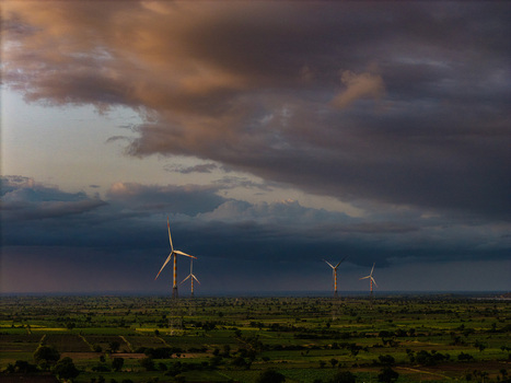 Aerial view of wind turbines standing in a vast green rural landscape under a dramatic stormy sky at sunset in Hampi Karnataka India.