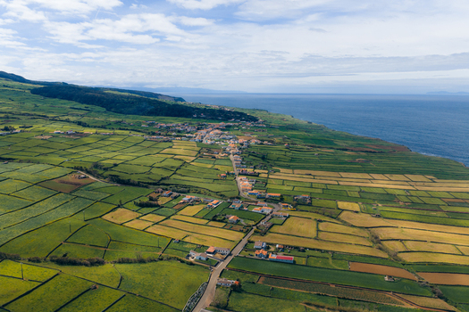 Aerial view of Terceira Island with its characteristic green patchwork fields and a coastal village under a cloudy sky Azores Portugal. Aerial view of Terceira Island with its characteristic green patchwork fields and a coastal village under a cloudy sky Azores Portugal.