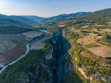 Aerial view of Osumi Canyon featuring steep limestone cliffs a winding river below and surrounding agricultural fields and forests in Dhores Berat County Albania.