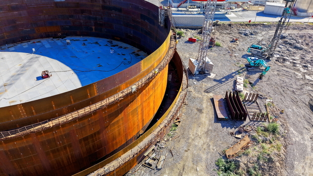 Aerial view of the assembly of a large circular metal oil storage tank at a refinery construction site with heavy machinery and excavators on the ground in Kovin Vojvodina Serbia. Aerial view of the assembly of a large circular metal oil storage tank at a refinery construction site with heavy machinery and excavators on the ground in Kovin Vojvodina Serbia.