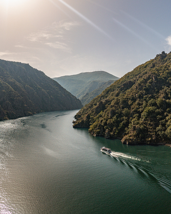Aerial view of Ribeira Sacra with a boat cruising on the Sil River surrounded by steep forested canyon walls under a bright sky Lugo Orense Spain. Aerial view of Ribeira Sacra with a boat cruising on the Sil River surrounded by steep forested canyon walls under a bright sky Lugo Orense Spain.