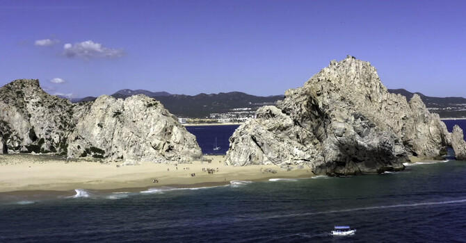 Aerial view of El Arco rock formation with sandy beach turquoise water and a small boat in Cabo San Lucas Baja California Sur Mexico.