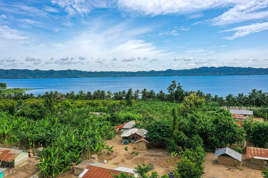 Aerial view of Lake Bosomtwe surrounded by lush green vegetation banana plantations and small rural houses under a bright blue sky in Bosomtwe Ashanti Region Ghana.