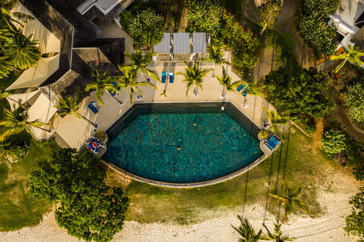 Aerial view of a semi circular swimming pool with people swimming surrounded by palm trees and sun loungers at a luxury resort in Mauritius Moka District Mauritius. Aerial view of a semi circular swimming pool with people swimming surrounded by palm trees and sun loungers at a luxury resort in Mauritius Moka District Mauritius.