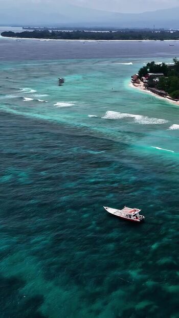 Aerial view of a boat in turquoise waters off the coast of Indonesia.