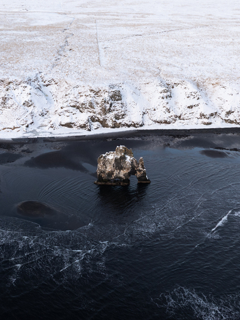 Aerial view of Hvitserkur sea stack surrounded by dark water and snow covered coastline in Iceland. Aerial view of Hvitserkur sea stack surrounded by dark water and snow covered coastline in Iceland.