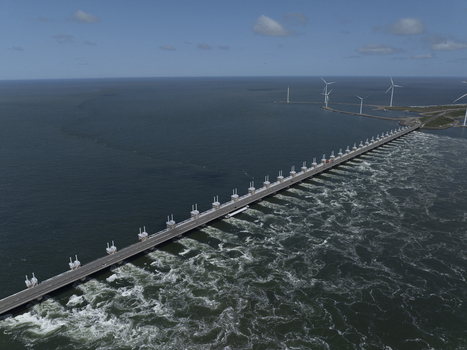 Aerial view of the Eastern Scheldt Storm Surge Barrier with turbulent water currents wind turbines in the distance and a clear blue sky in Vrouwenpolder Zeeland Netherlands. Aerial view of the Eastern Scheldt Storm Surge Barrier with turbulent water currents wind turbines in the distance and a clear blue sky in Vrouwenpolder Zeeland Netherlands.