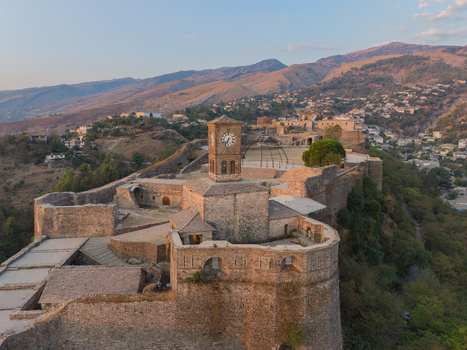 Aerial view of the historic Gjirokaster Fortress featuring its iconic clock tower and stone fortifications set against a mountainous landscape in Gjirokaster Gjirokaster County Albania. Aerial view of the historic Gjirokaster Fortress featuring its iconic clock tower and stone fortifications set against a mountainous landscape in Gjirokaster Gjirokaster County Albania.