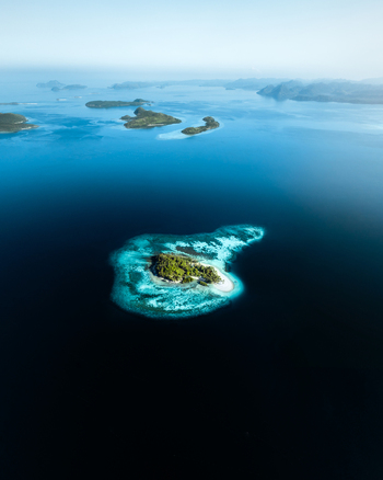 Aerial view of a small tropical island surrounded by turquoise coral reefs and deep blue ocean waters in Coron Mimaropa Philippines.