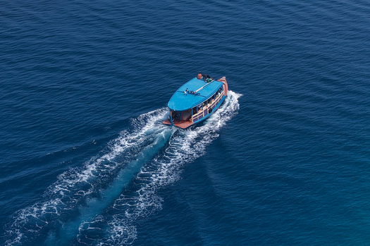 Aerial view of a blue boat cruising through the deep blue waters of the Indian Ocean leaving a white wake behind it in Kulhudhuffushi Haa Dhaalu Atoll Maldives.