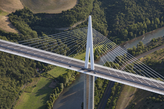 Aerial view of the Millau Viaduct bridge pierces the sky a stark white contrast against the verdant valley and winding river Millau France. Aerial view of the Millau Viaduct bridge pierces the sky a stark white contrast against the verdant valley and winding river Millau France.