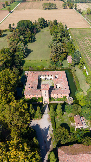 Aerial view of Castello di Peschiera Borromeo with its brick architecture courtyard and moat surrounded by trees and fields in Peschiera Borromeo Lombardy Italy.