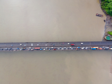 Aerial view of a bridge spanning a wide river with heavy traffic including cars and trucks with boats moored along the muddy riverbank in Thane Maharashtra India. Aerial view of a bridge spanning a wide river with heavy traffic including cars and trucks with boats moored along the muddy riverbank in Thane Maharashtra India.