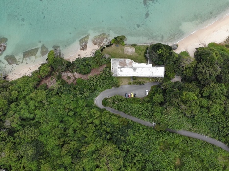 Aerial view of the Hyakume coastline with a building in lush greenery a winding road with parked cars and a sandy beach meeting the emerald sea in Nanjo Okinawa Japan. Aerial view of the Hyakume coastline with a building in lush greenery a winding road with parked cars and a sandy beach meeting the emerald sea in Nanjo Okinawa Japan.