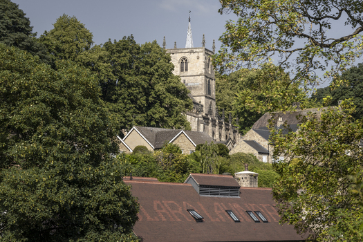 View of the historic St John the Baptist Church tower rising above lush green trees and stone rooftops in Knaresborough England United Kingdom.